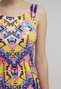 Robe sans manches avec des motifs géométriques et abstraits colorés en rose, jaune, bleu, noir et blanc sur le haut du torse d'une personne.