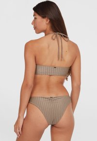 Top de bikini marrón con canalé y lazo en la parte posterior, junto con la parte inferior a juego. La tela tiene una textura suave con sutiles rayas verticales.