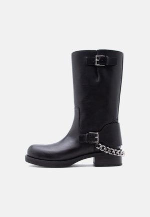 Μαύρο δερμάτινο μπότες μέσης γάμπας με δύο ασημένιες αγκράφες και λεπτομέρεια ασημένιας αλυσίδας που τυλίγεται γύρω από την φτέρνα σε χαμηλή φιάπα σόλα.