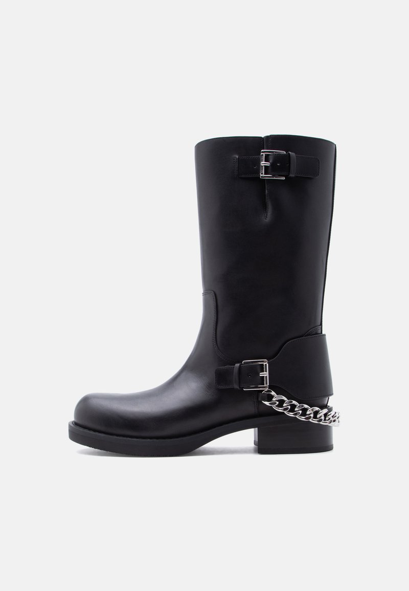 Μαύρο δερμάτινο μπότες μέσης γάμπας με δύο ασημένιες αγκράφες και λεπτομέρεια ασημένιας αλυσίδας που τυλίγεται γύρω από την φτέρνα σε χαμηλή φιάπα σόλα.
