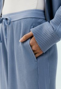 Blauw textiel kledingstuk van ribbelstof, met een tailleband en een getrokken koord. Inclusief zijzakken en een ontspannen pasvorm.