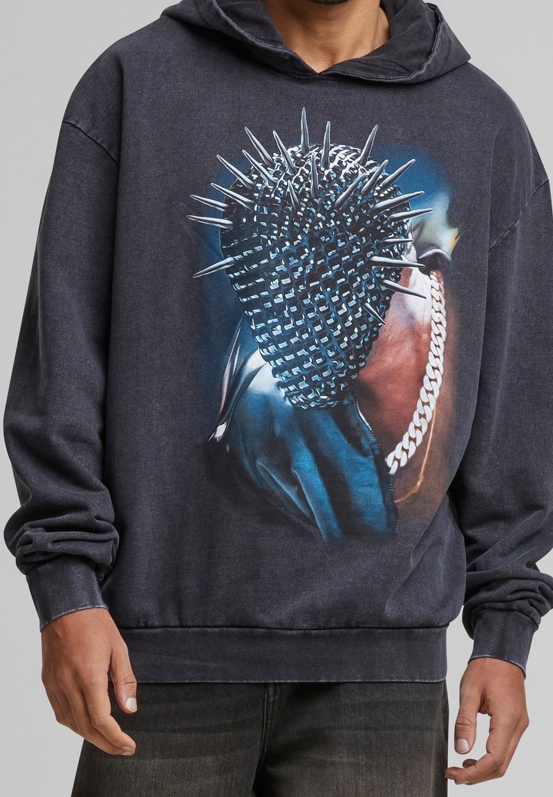 Donkergrijze hoodie met een afbeelding van een gespikkelde microfoon met een kettingdetail. De stof ziet er zacht uit, heeft een ontspannen pasvorm en lange mouwen.