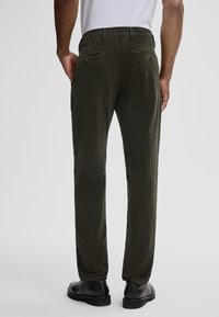 Donkergroene corduroy broek met een gestructureerd oppervlak, twee achterzakken en een elastische tailleband. Draagt met zwarte enkellaarzen.
