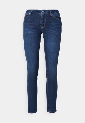 Tummansininen slim fit farkut, joissa on etunappi ja taskut, esitettynä tasaisesti valkoista taustaa vasten.