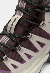 Μπότα πεζοπορίας Salomon με σχεδιασμό σε μπορντό και γκρι, μαύρα κορδόνια με πουά, υφή από δίχτυ και μωβ λεπτομέρειες στη σόλα και στα πλαϊνά.