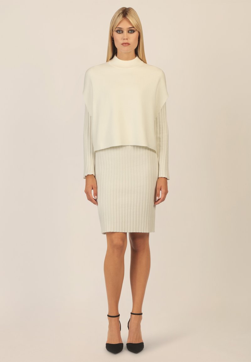Maglione grigio chiaro a maglia con collo alto e design cropped abbinato a una gonna a matita a coste dello stesso colore. Tacchi neri con cinturino alla caviglia completano il look.