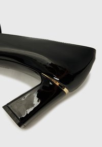 Black patent leather high heel with a chunky heel. Features a gold accent on the heel and a smooth, glossy surface.