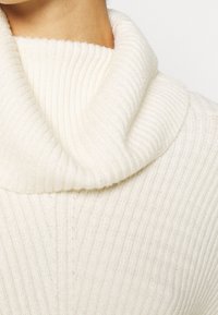 Weißer, gerippter Rollkragenpullover mit engem, umgeschlagenem Kragen und einer weichen Textur mit vertikalen Linien.