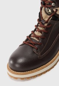 Brown leather hiking boot with a textured finish, brown laces, beige lining, and a rugged sole with a wood-like appearance.