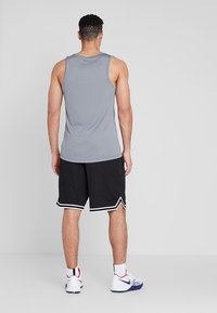 Camiseta sin mangas gris, pantalones cortos deportivos negros con detalles en blanco y zapatillas deportivas. Diseño simple, material ligero.
