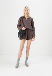 Brun zip-up hettegenser, matchende shorts, grå sokker og beige hæler. Svart crossover-veske med frynse-detaljer. Enkel, avslappet passform.