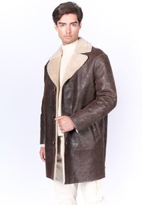 Chaqueta de cuero marrón con un collar de borreguito beige, cierre de botones y bolsillos laterales. Textura suave con un acabado ligeramente brillante.