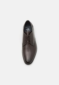 Chaussure habillée en cuir marron avec une finition lisse et brillante, dotée d'un système de laçage et d'un design large pour le confort. Semelle plate avec des coutures discrètes.