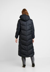 Long dark navy puffer coat with a hood, chevron stitching, and side panels. Smooth texture and knee-length design.