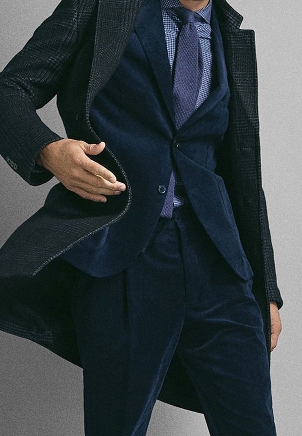 Costume bleu marine en tissu texturé, comprenant un blazer ajusté, un gilet et un pantalon slim. Cravates à motif contrastant, mettant en valeur un look soigné.