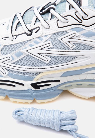 Κοντινό πλάνο sneaker σε ανοιχτό μπλε και λευκό χρώμα με μαύρες λεπτομέρειες, πλευρές από λεπτό δίχτυ και διπλωμένο κορδόνι σε ανοιχτό μπλε χρώμα δίπλα του.
