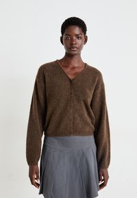 Cardigan marrone e morbido con scollo a V e cinque bottoni frontali, abbinato a una gonna grigia a pieghe. Texture soffice e vestibilità rilassata.