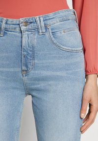 Valkoiset siniset farkut korkealla vyötäröllä, viisi taskua ja hienovarainen kulutuskuvio. Kontrastivärinen ommel ja etupainike.