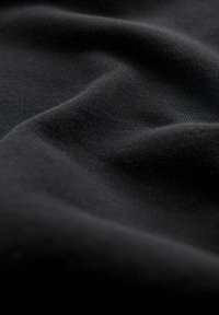 Gros plan sur un tissu noir doux avec une texture tricotée visible et des plis délicats créant des ombres et des reflets.