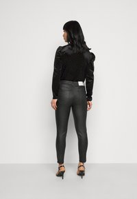 Blusa de veludo preta com mangas bufantes e padrão de bolinhas, combinada com calças pretas de corte justo e sapatos de salto alto pretos com tiras.