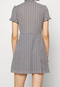 Schwarz-weißes Gingham-Kleid mit kurzen puffärmel, einem rüschend Kragen und einem ausgestellten Rock. Leichtes Material mit einem strukturierten Karomuster.