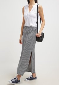 Un haut sans manches blanc et une jupe maxi rayée grise avec une fente sur le côté, associés à des baskets bleu marine et un petit sac à bandoulière noir.