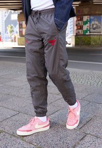 Grå lätta joggers med röda Jordan- och Bulls-logotyper, avslutade med ett elastiskt midjeband. Matchas med rosa Nike-skor och vita strumpor.