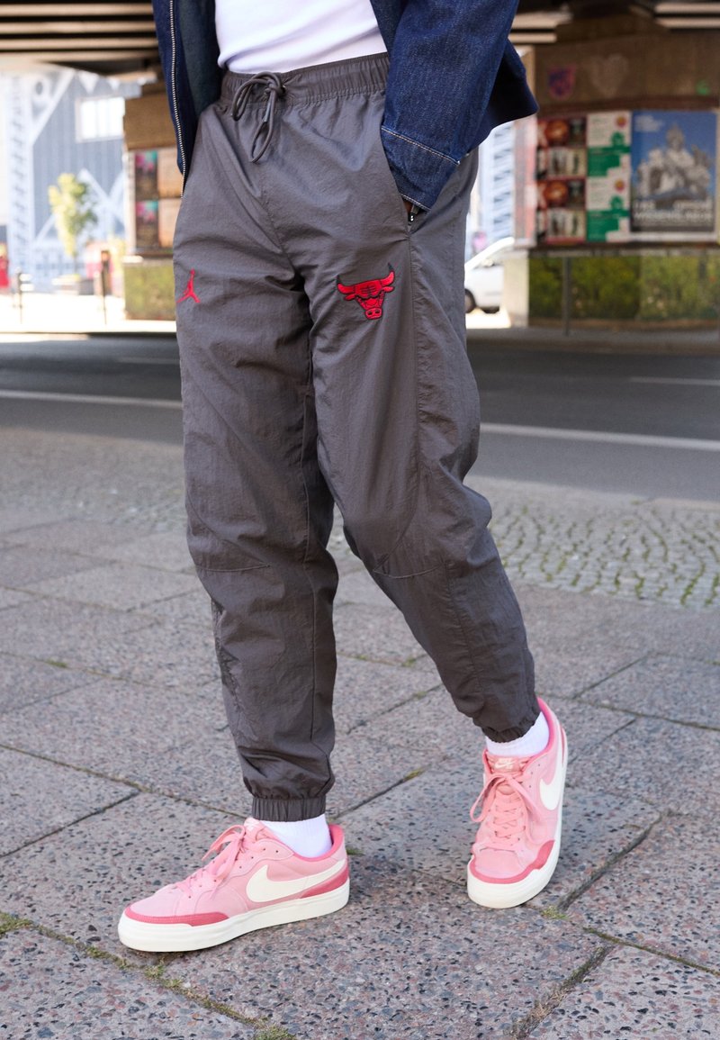 Graue, leichte Jogginghosen mit roten Jordan- und Bulls-Logos, abgeschlossen mit einem elastischen Bund. Dazu pinke Nike-Schuhe und weiße Socken.