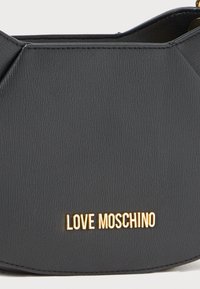 Melnā mākslīgā ādas rokassoma ar teksturētu virsmu. Ievērojams ar zelta "LOVE MOSCHINO" logotipu un strukturētu, leņķveida dizainu.