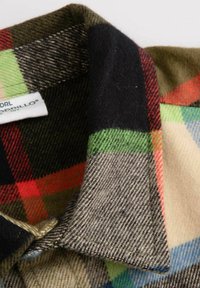 Koszula flanelowa w wielokolorowy wzór w kratkę, zawierająca czarne, czerwone, zielone i niebieskie kwadraty, oraz stożkowy kołnierz wykonany z miękkiego materiału.