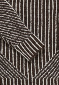 Manche de pull en laine rayée marron et blanche posée sur le corps, montrant en gros plan des motifs de maille verticaux et diagonaux.