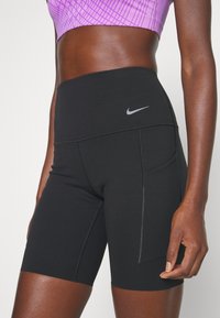 Shorts de sport noirs avec une taille haute, dotés d'une poche latérale, de détails de couture et d'un petit logo Nike gris. Fabriqués en matériau extensible.