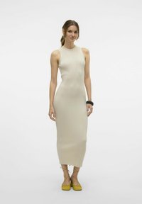 Abito midi a costine senza maniche in beige chiaro con una silhouette aderente. Abbinato a scarpe gialle con lacci alla caviglia, che mostrano un tessuto testurizzato.