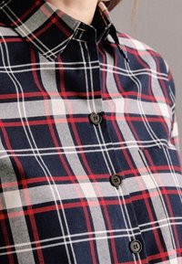Navy and red plaid shirt made of cotton, featuring a button-down collar, black buttons, and a single breast pocket detail.