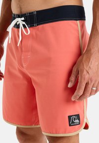 Korálové plavky s námořnickým páskem, nastavitelnou šňůrkou, bílým prošíváním a béžovými detaily; zahrnují logo na levém stehně.