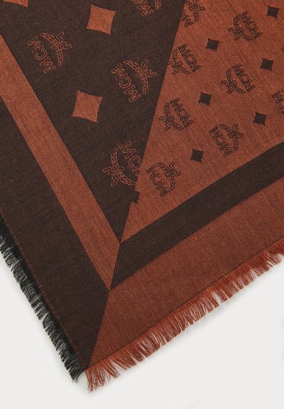 Écharpe marron à motif présentant un design géométrique avec des logos MCM, des bords frangés et une texture indicative d'un tissu tissé.