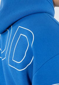 Blauwe hoodie met witte contourtekst, gemaakt van zacht katoen, licht gestructureerde stof, met een capuchon en afgeronde schoudernahts.