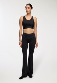 Reggiseno sportivo nero con pannelli laterali testurizzati, abbinato a leggings neri a vita alta e a campana in tessuto elasticizzato, con una finitura liscia.