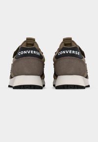 Ζευγάρι καφέ και μπεζ αθλητικών παπουτσιών Converse, εμφανιζόμενα από πίσω, με μαύρες ταμπέλες στη φτέρνα που φέρουν λευκή σήμανση Converse.