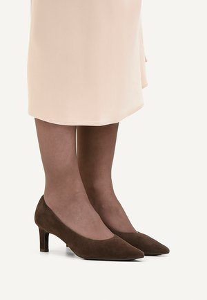 Beine, die transparente braune Strumpfhosen und braune Wildleder-Pumps mit niedrigem Absatz tragen, kombiniert mit einem hellbeigen Rock.