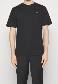 Černé bavlněné tričko s krátkými rukávy, kulatým výstřihem a decentním logem na hrudi. Hladká textura a přiléhavý střih.