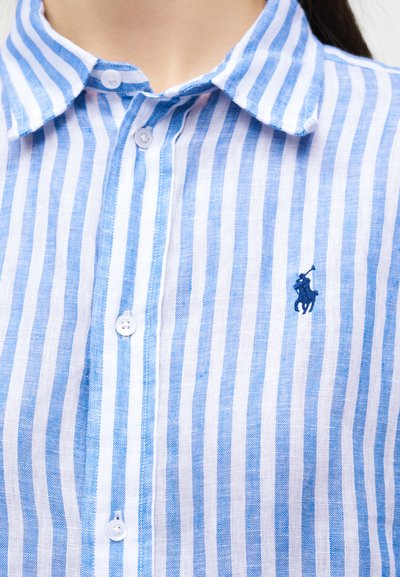 Gros plan sur une chemise à boutons à rayures verticales bleues et blanches avec col et logo brodé d'un joueur de polo sur la poitrine.