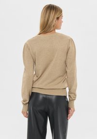 Svijetlosmeđi pleteni pulover s okruglim dekolteom, nabranim rukavima i rebrastim rubom. Nositi uz uske crne kožne hlače.