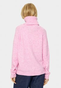 Rožinė, megzta palaidinė su aukštu, sulenktu apykakle. Per didelis kirpimas, raukšlėtos rankovės ir apatinė dalis, su minkšta tekstūra ir minimalistiniu dizainu.