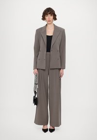 Grau maßgeschneiderter Anzug mit weit geschnittenen Hosen, einem doppelt geknöpften Blazer und einem schwarzen Oberteil. Enthält eine kleine schwarze Handtasche mit einem Umhängeriemen.