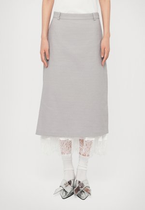 Jupe midi grise sur ourlet en dentelle blanche, portée avec des chaussettes blanches et des chaussures argentées pointues brillantes avec de grands nœuds.