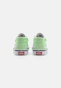 Zapatillas altas verdes de gamuza con acentos blancos, cuello acolchado, dobles correas y el logotipo rojo de Vans en el talón. Suela de goma.