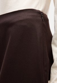 Jupe en tissu marron avec une surface texturée, dotée d'une fermeture éclair sur le côté, accompagnée d'une chemise de couleur claire.