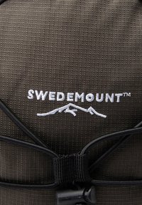 Brązowy plecak teksturowany z tkaniny z białym logo "SWEDEMOUNT" i grafiką górską, z czarnymi sznurkami i detalem z złączkami.