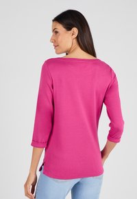 Top de manga larga fucsia con puños enrollados, escote barco y aberturas laterales; hecho de una tela suave y lisa con una forma ajustada.